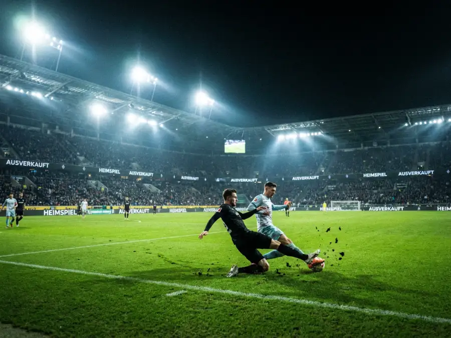 Fußballspiel bei Flutlicht in einem ausverkauften Stadion bei Nacht mit grünem Rasen und Spielern auf dem Feld