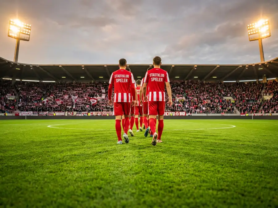 Fußballspieler in rotem und weißem Trikot auf dem Rasen eines großen Stadions während eines Turnierspiels
