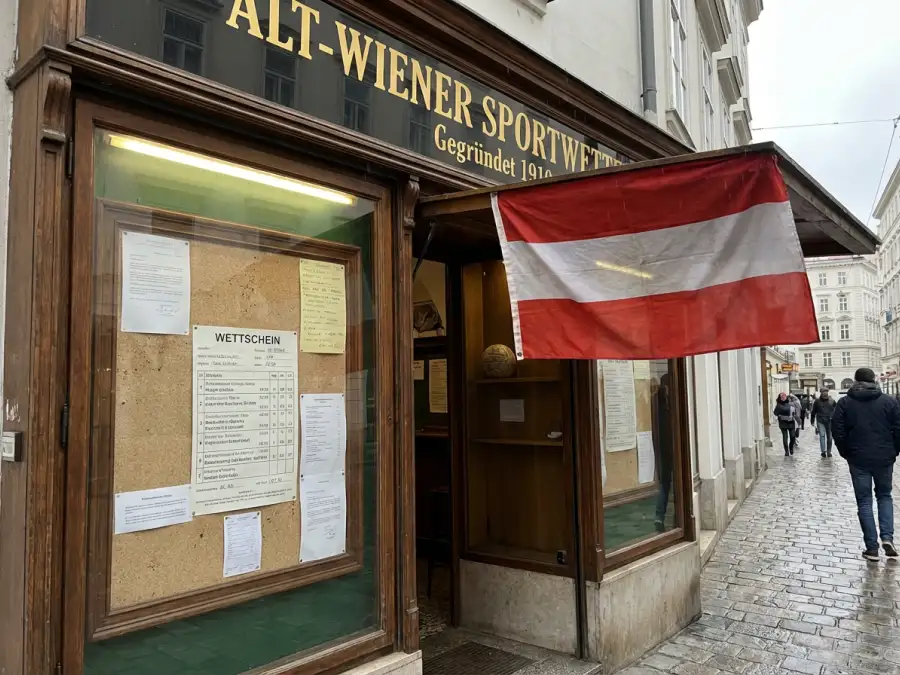 Österreichische Flagge und ein Wettschein mit Dezimalquoten vor dem Hintergrund eines Wiener Wettbüros